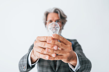 With light bulb in hands. Senior stylish modern man with grey hair and beard indoorsの写真素材