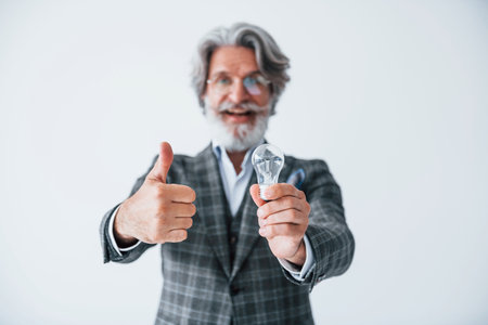 With light bulb in hands. Senior stylish modern man with grey hair and beard indoorsの写真素材