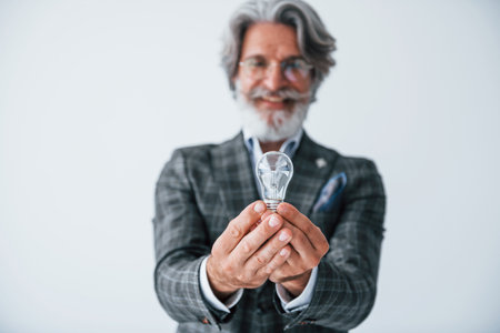 With light bulb in hands. Senior stylish modern man with grey hair and beard indoorsの写真素材