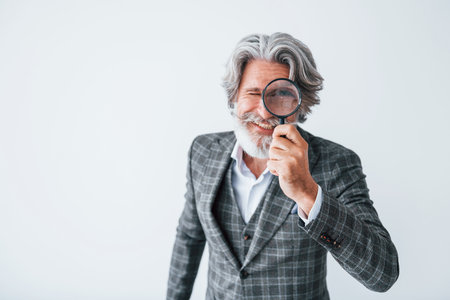 Having fun with magnifying glass. Senior stylish modern man with grey hair and beard indoorsの写真素材