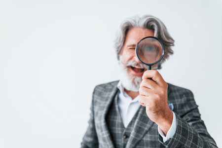 Having fun with magnifying glass. Senior stylish modern man with grey hair and beard indoorsの写真素材
