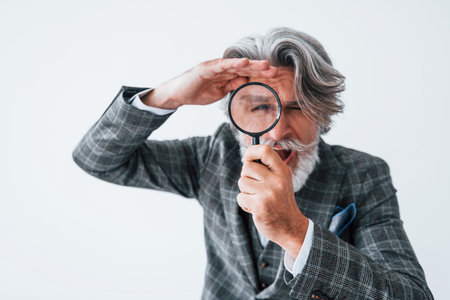 Having fun with magnifying glass. Senior stylish modern man with grey hair and beard indoorsの写真素材