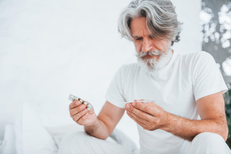 Feels sick. On the bed. Senior stylish modern man with grey hair and beard indoorsの写真素材