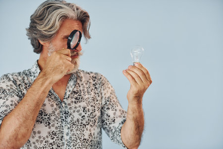 Having fun with magnifying glass. Senior stylish modern man with grey hair and beard indoorsの写真素材