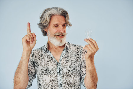 Holds light bulb in hands. Conception of ideas and inspiration. Senior stylish modern man with grey...