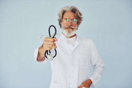 Doctor in white coat against wall. Senior stylish modern man with grey hair and beard indoorsの写真素材