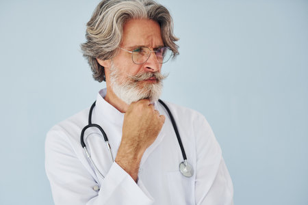 Doctor in white coat against wall. Senior stylish modern man with grey hair and beard indoorsの写真素材