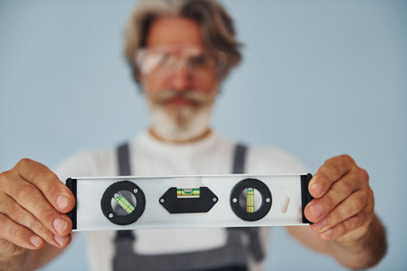 Worker in uniform holds level matching device. Senior stylish modern man with grey hair and beard indoorsの写真素材