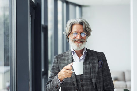 Takes a break and drinks coffee. Senior stylish modern man with grey hair and beard indoorsの写真素材