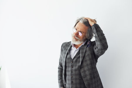 Posing for a camera while standing against white background. Senior stylish modern man with grey hair and beard indoorsの写真素材