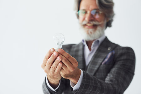 Posing for a camera while standing against white background. Senior stylish modern man with grey hair and beard indoorsの写真素材