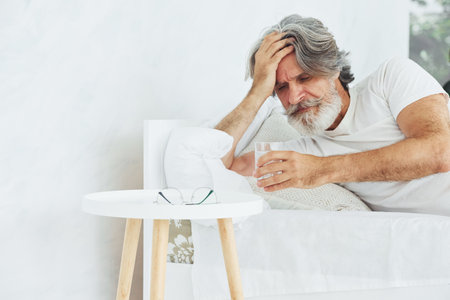 Conception of illness and virus. Senior stylish modern man with grey hair and beard indoorsの写真素材