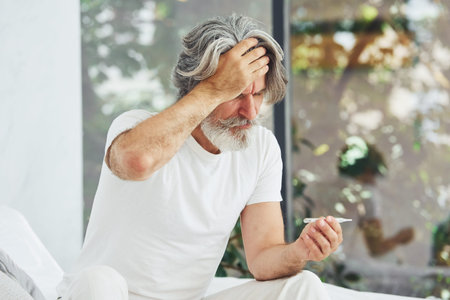 Conception of illness and virus. Senior stylish modern man with grey hair and beard indoors