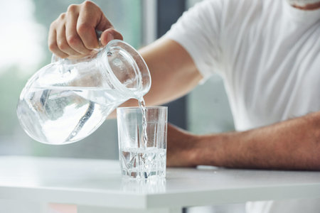 Close up view of man that sits by table and pouring water into glass