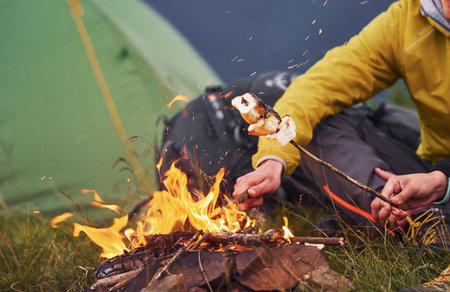 Close up view of peoples hands that holds sticks with marshmallow outdoors near campfire