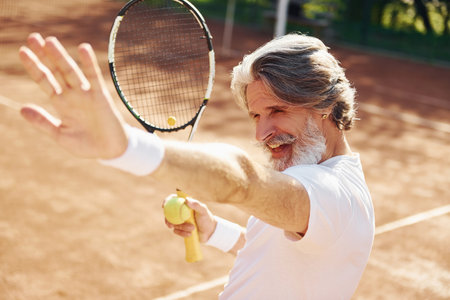 Celebrating victory. Senior modern stylish man with racket outdoors on tennis court at daytimeの写真素材