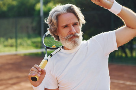 Senior modern stylish man with racket outdoors on tennis court at daytimeの写真素材