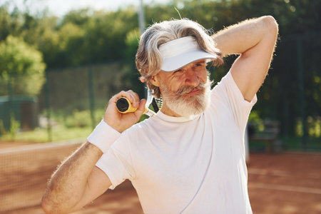 Senior modern stylish man with racket outdoors on tennis court at daytimeの写真素材