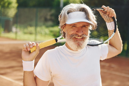 Senior modern stylish man with racket outdoors on tennis court at daytimeの写真素材