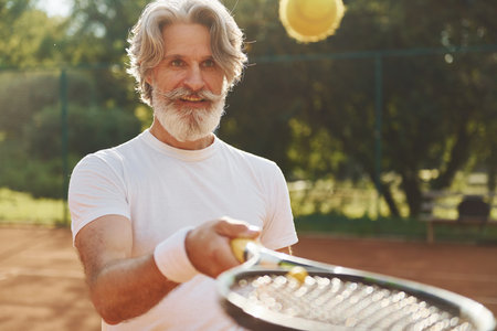 Training time. Senior modern stylish man with racket outdoors on tennis court at daytimeの写真素材