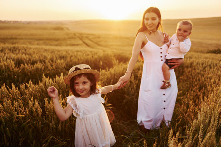 Cheerful family of mother, little son and daughter spending free time on the field at sunny day time of summerの写真素材