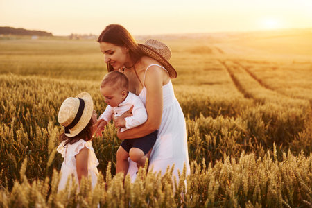 Cheerful family of mother, little son and daughter spending free time on the field at sunny day time of summerの写真素材
