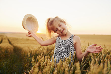 Little girl standing on the agricultural field at evening time. Conception of summer free timeの写真素材