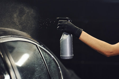 Spraying the vehicle. Modern black automobile get cleaned by woman inside of car wash stationの写真素材