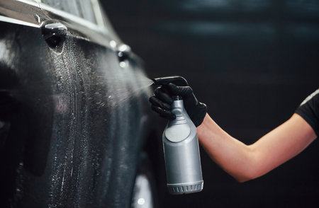 Spraying the vehicle. Modern black automobile get cleaned by woman inside of car wash stationの写真素材