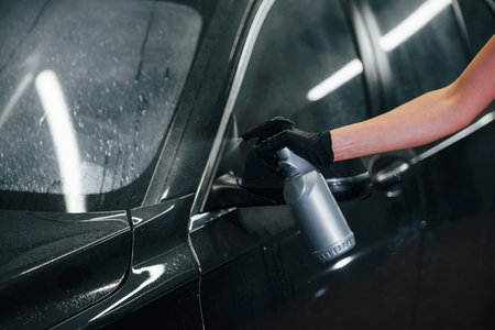 Spraying the vehicle. Modern black automobile get cleaned by woman inside of car wash stationの写真素材