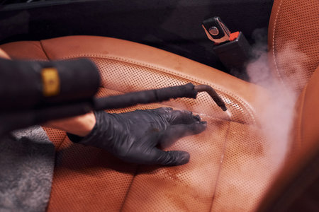 Uses steam cleaner. Modern black automobile is in service by woman inside of car wash stationの写真素材