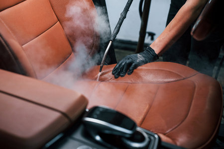 Uses steam cleaner. Modern black automobile is in service by woman inside of car wash stationの写真素材