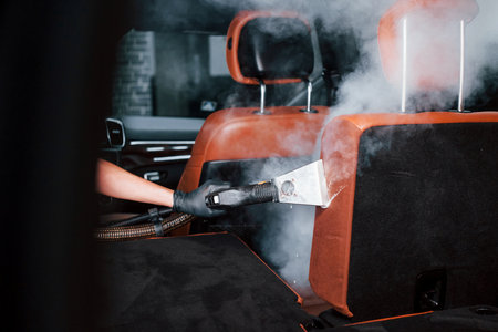 Uses steam cleaner. Modern black automobile is in service by woman inside of car wash stationの写真素材