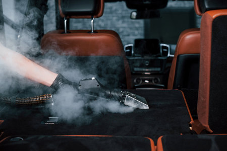 Uses steam cleaner. Modern black automobile is in service by woman inside of car wash stationの写真素材