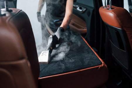 Uses steam cleaner. Modern black automobile is in service by woman inside of car wash stationの写真素材