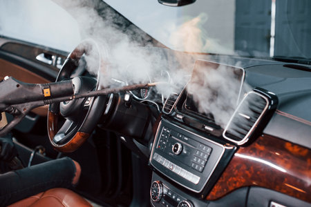 Modern black automobile get cleaned inside by steam equipment by worker inside of car wash stationの写真素材