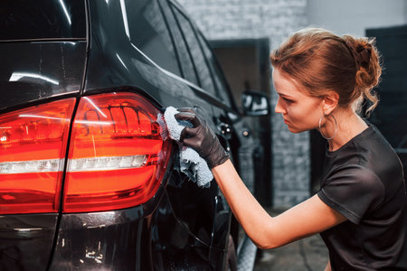 Final polishing. Modern black automobile get cleaned by woman inside of car wash stationの写真素材