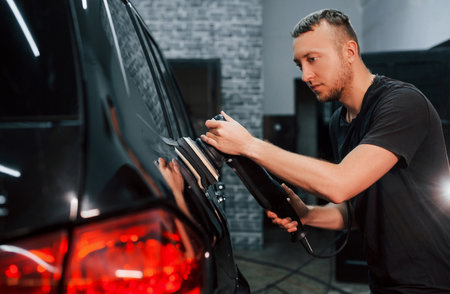 Guy polishing surface of vehicle. Modern black automobile get cleaned by man inside of car wash stationの写真素材