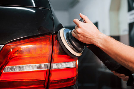 Guy polishing surface of vehicle. Modern black automobile get cleaned by man inside of car wash stationの写真素材