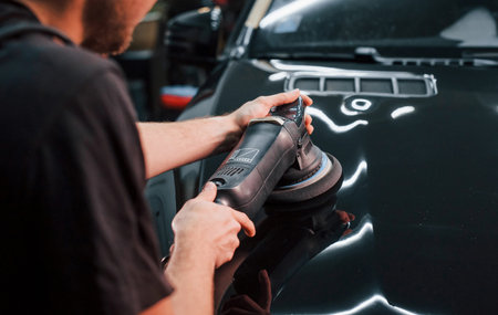Guy polishing surface of vehicle. Modern black automobile get cleaned by man inside of car wash...