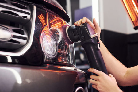 Guy polishing surface of vehicle. Modern black automobile get cleaned by man inside of car wash...