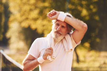 Senior stylish man in white shirt and black sportive shorts on tennis courtの写真素材