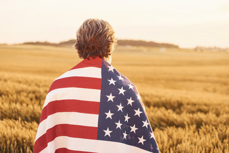 View from behind of patriotic senior man that standing on the field with USA flag. Conception of freedomの写真素材
