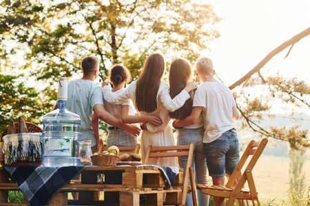 Embracing each other and looking at sunset. Group of young people have vacation outdoors in the forest. Conception of weekend and friendshipの写真素材