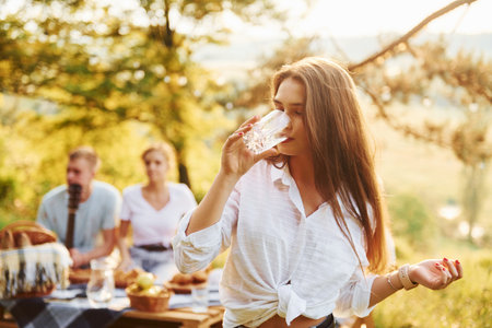 Girl with glass of water. Group of young people have vacation outdoors in the forest. Conception of weekend and friendshipの写真素材