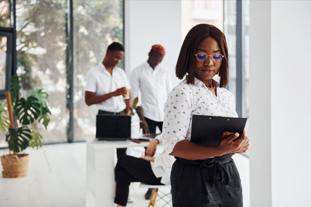 Beautiful woman in glasses in front of her colleagues. Group of african american business people working in office togetherの写真素材