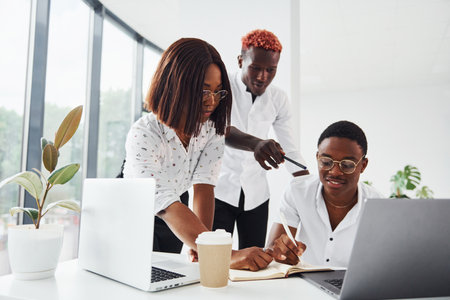 Using same laptop for the project. Group of african american business people working in office togetherの写真素材