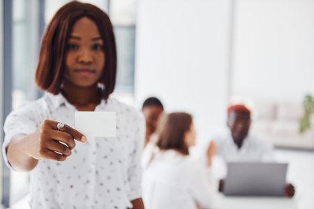 Woman holds business card card. Group of african american people working in office togetherの写真素材