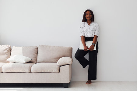 Young african american woman in formal clothes standing with laptop in hands indoorsの写真素材