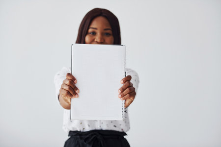 Young african american woman in formal clothes standing with notepad and empty paper in hands indoorsの写真素材